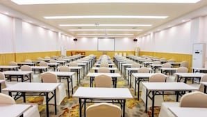 A conference room with rows of tables and chairs, a projector screen, and a carpeted floor. - Yili Hotel (Kaiping)