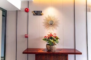 Un mostrador de recepción con una planta en maceta, un cartel con números en la pared y una lámpara decorativa con motivos de sol.