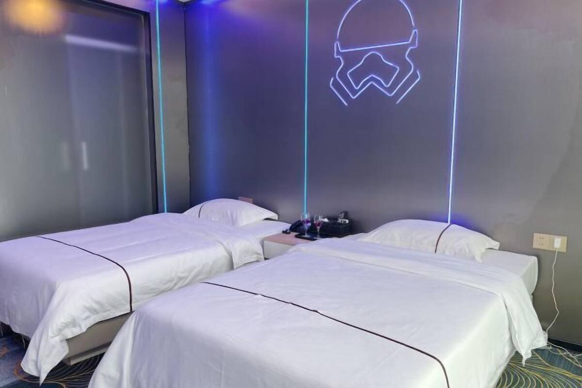 A hotel room with two beds, a Star Wars-themed neon light, and a window with blinds.