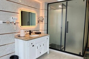 A modern bathroom with a white vanity, a round mirror, a hairdryer, and a glass-enclosed shower.