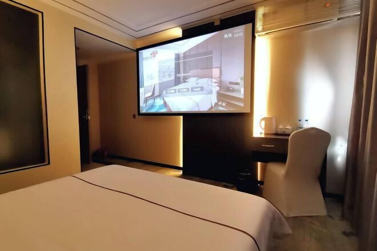A hotel room with a bed, a desk, a chair, and a television displaying a room layout.