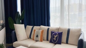 A sofa with three cushions, a large plant, and a window with curtains. - Yili Hotel (Kaiping)
