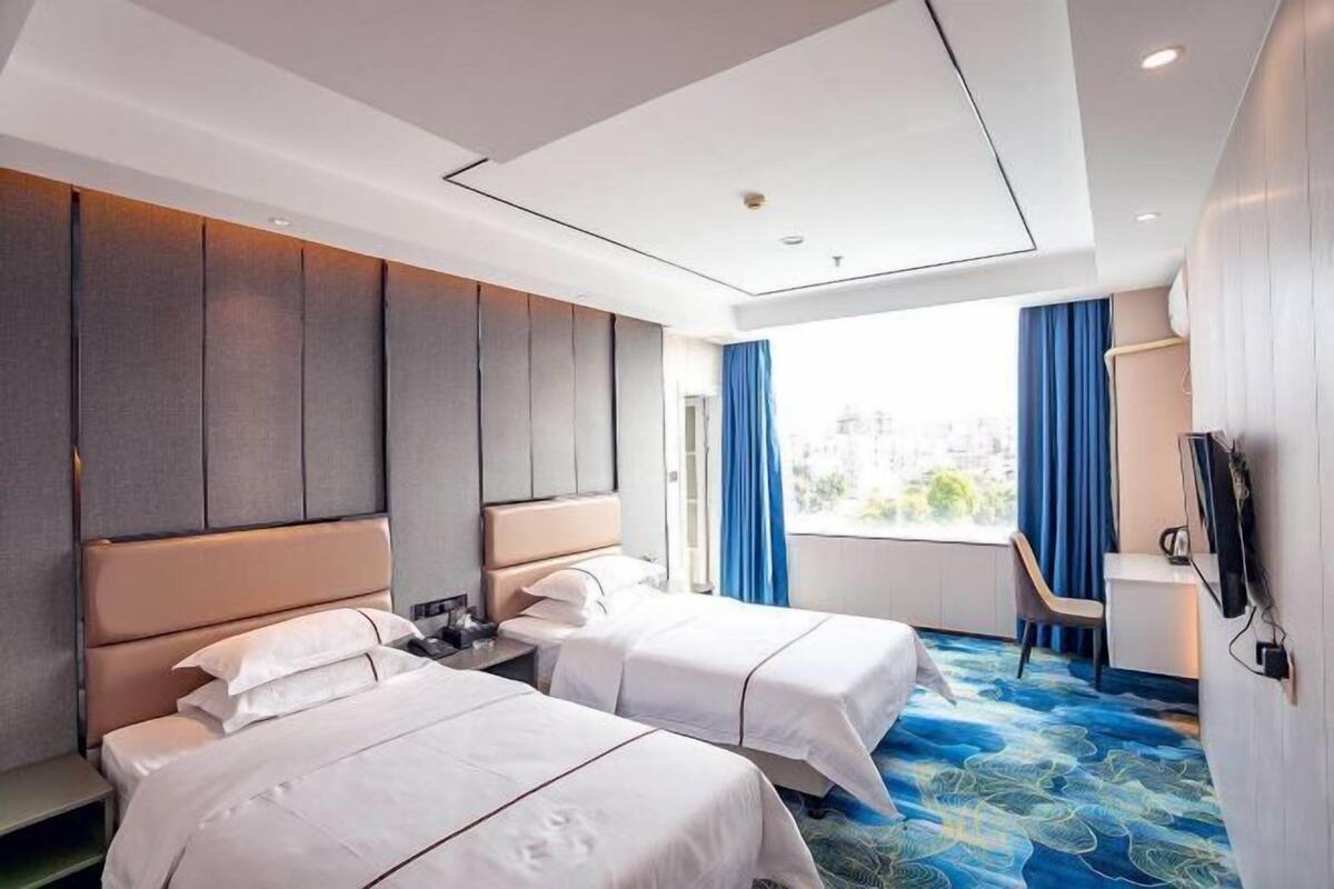 A hotel room with two beds, a desk, a chair, and a large window with curtains.
