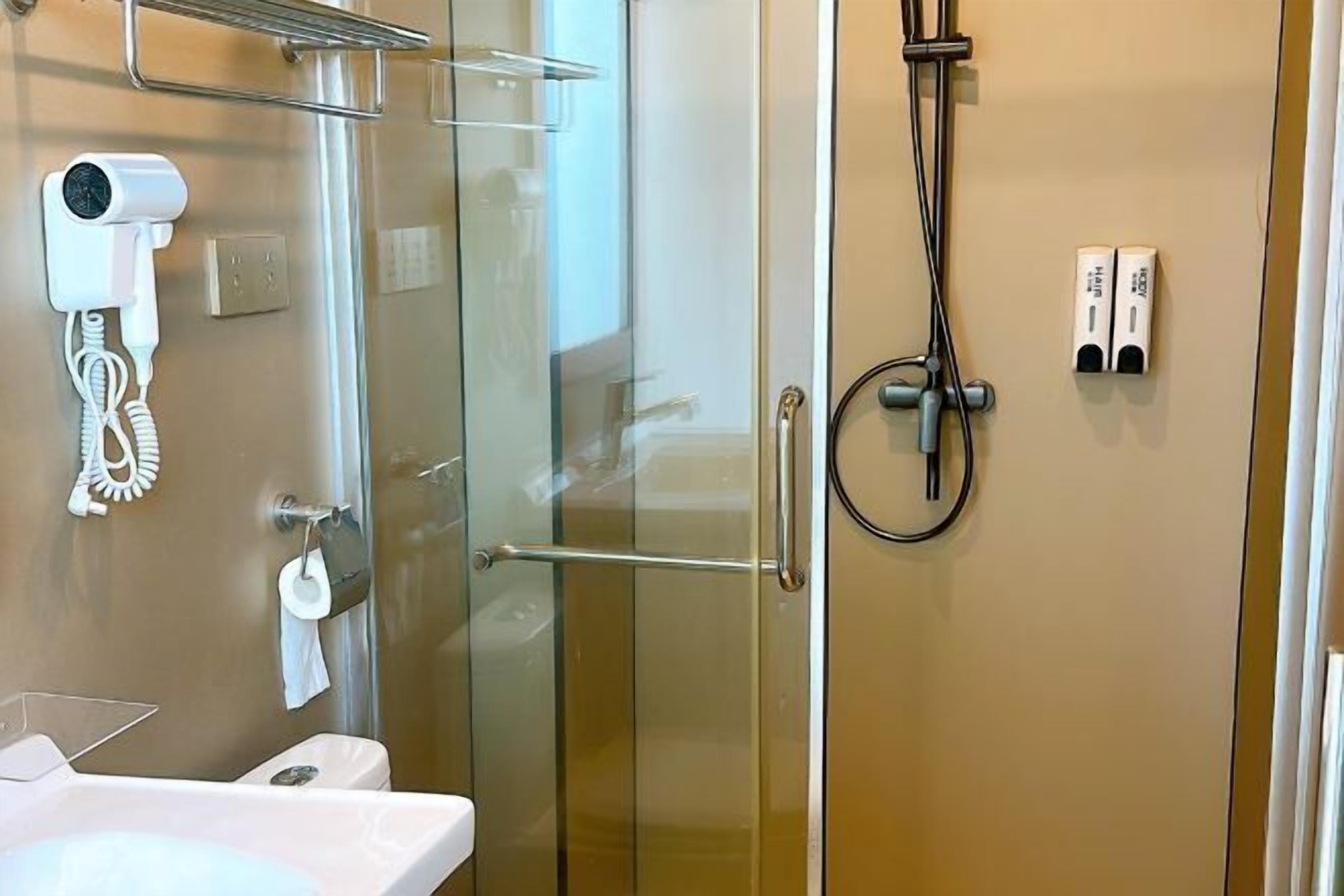 A modern bathroom with a glass shower enclosure, a hairdryer, and toiletries on the wall.