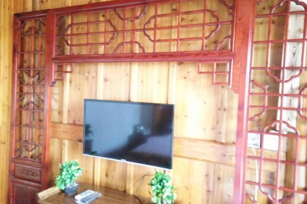 A room with wooden paneling, a mounted flat-screen TV, and two potted plants on a wooden table.
