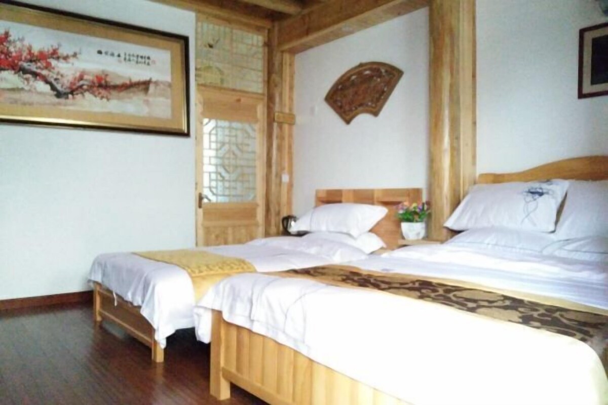 A room with two wooden beds, a wooden floor, a framed painting, and a decorative fan.