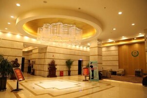 Un hall de hotel con una gran lámpara de araña, suelo de mármol y una recepción.