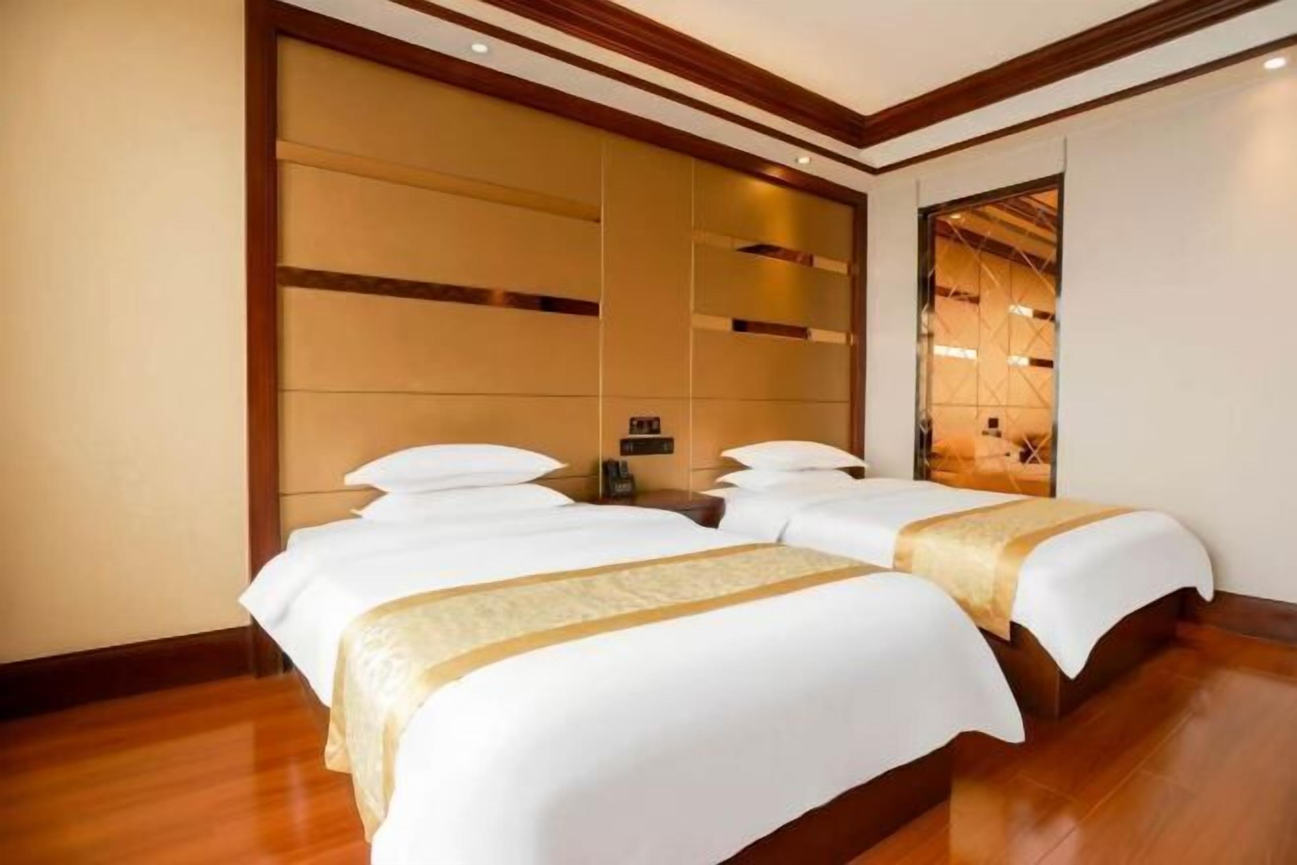 Habitación de hotel con dos camas, un espejo grande y piso de madera.