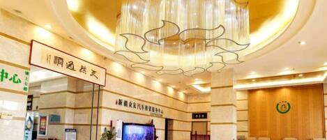 A hotel lobby with a large chandelier, a reception desk, and a television screen.