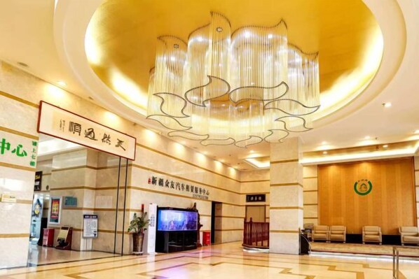 A hotel lobby with a large chandelier, a reception desk, and a television screen.