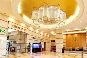 A hotel lobby with a large chandelier, a reception desk, and a television screen.