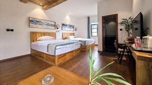 A room with two wooden beds, a wooden desk, and a chair. There is a plant on the desk and a painting on the wall.