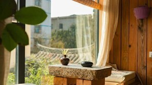 A room with a wooden bench, a small table with a plant, and a view of traditional architecture through a window.