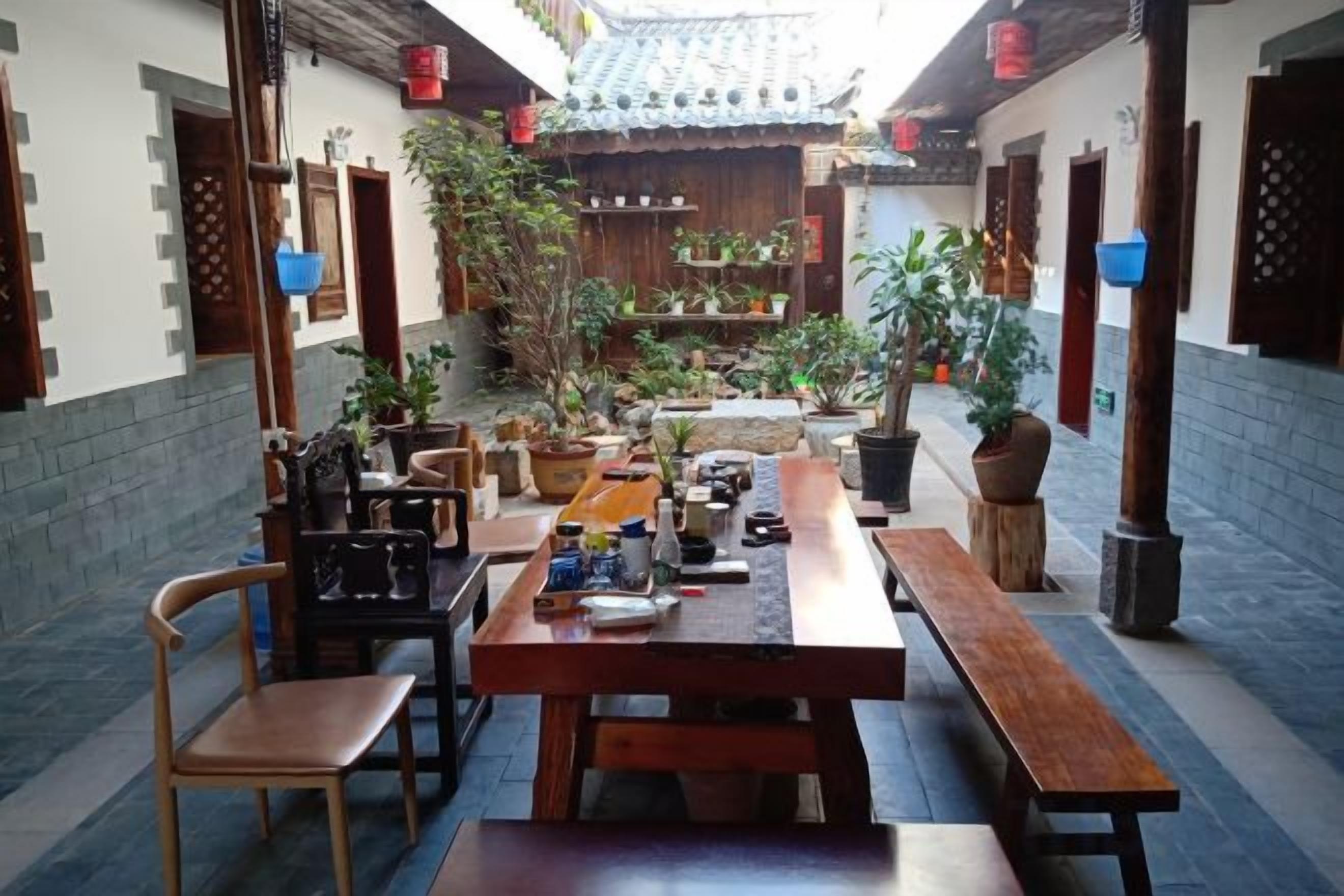 Un patio tradicional con bancos y mesas de madera, rodeado de plantas en macetas y un techo de tejas.