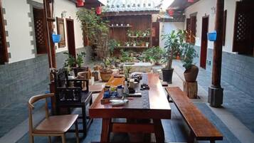 Un patio tradicional con bancos y mesas de madera, rodeado de plantas en macetas y un techo de tejas.