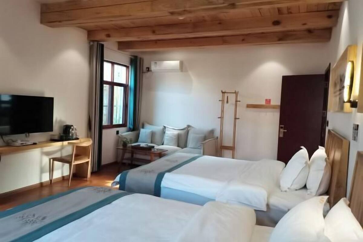 Et hotelværelse med to senge, et skrivebord med fjernsyn, en stol, et vindue og et træloft.