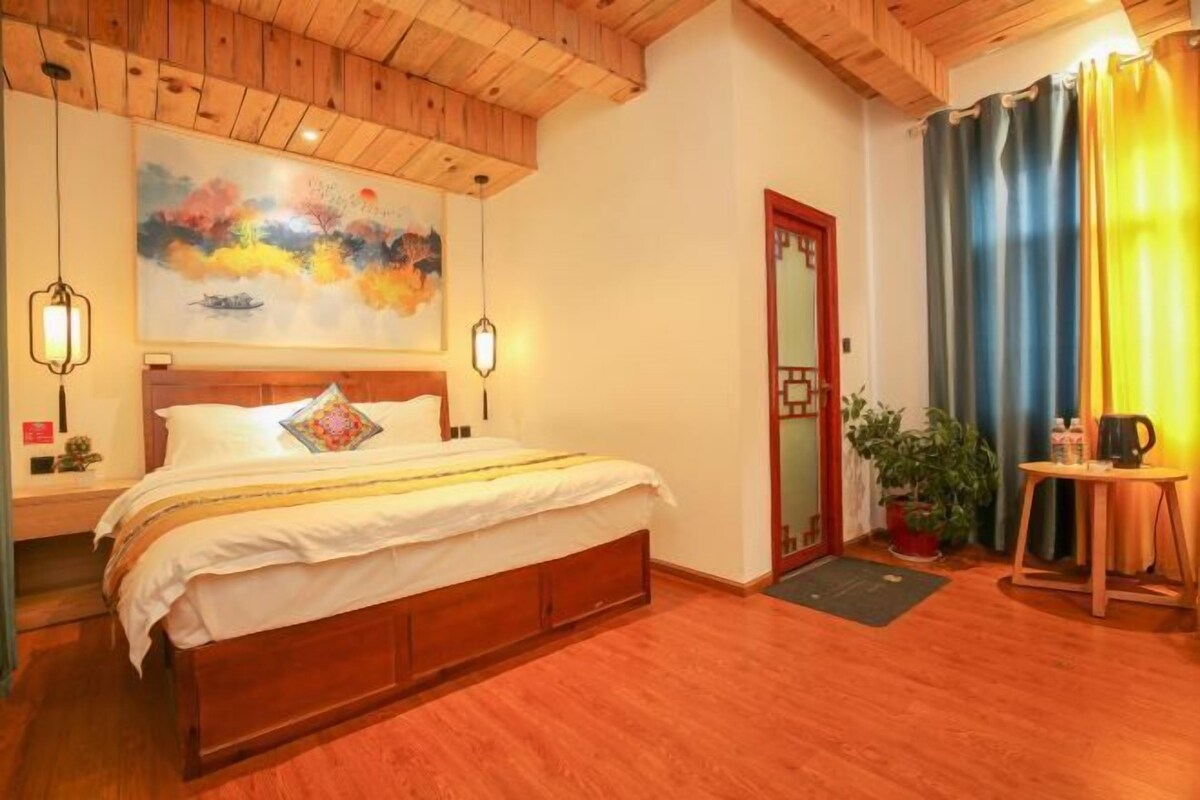 A bedroom with a wooden ceiling, a bed with white bedding, a painting above the bed, a door with a mirror, and a curtain on the window.