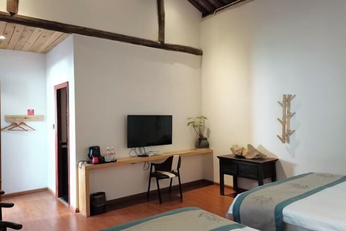 A room with two beds, a desk with a TV, a chair, and a small table.