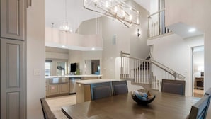 A modern kitchen with a central island, a dining area with a wooden table, and a staircase leading to an upper level. - New Listing Ozark Views at Majestic - Perched on the Hills (Branson)