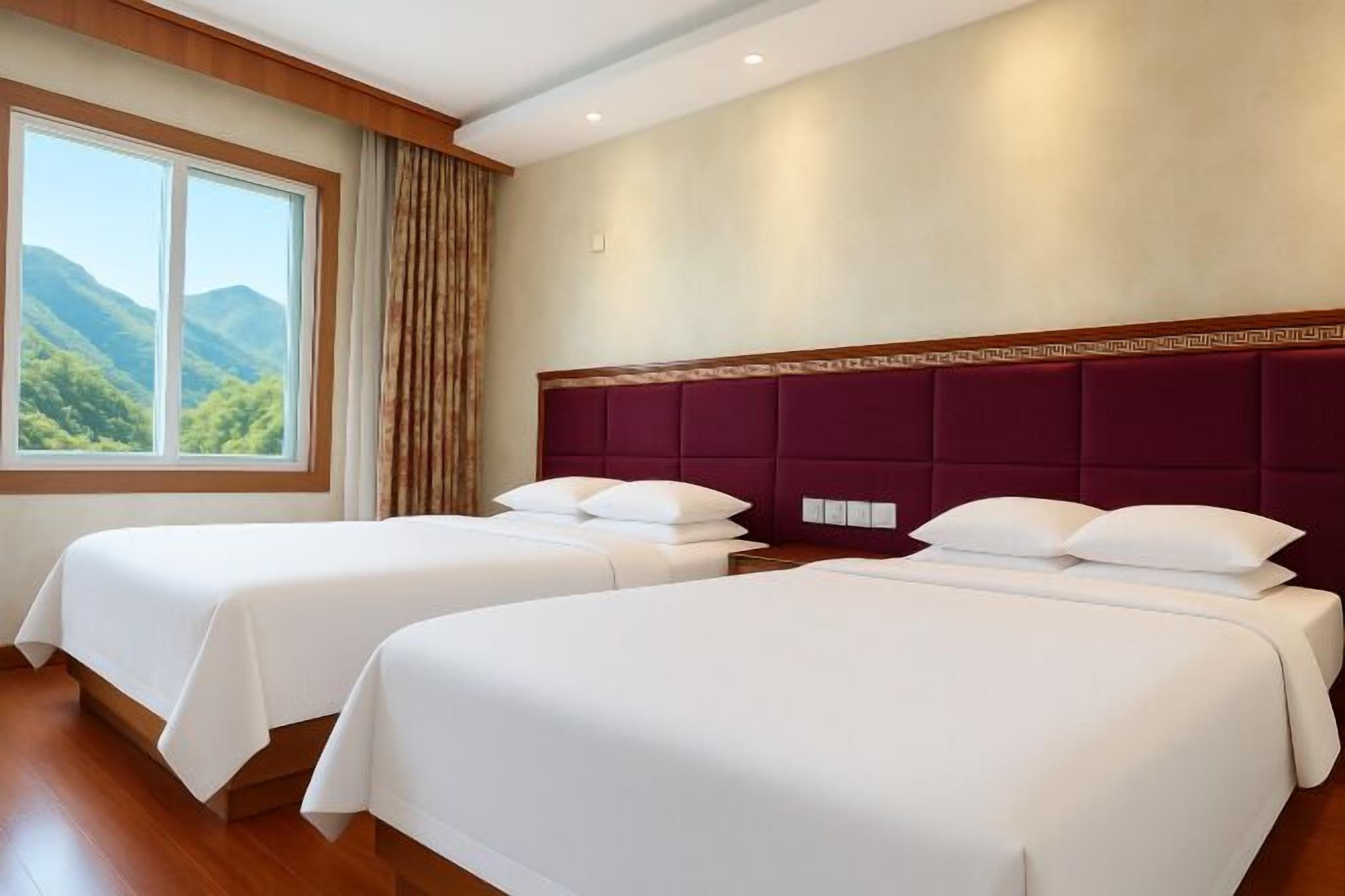 Une chambre d’hôtel avec deux lits, une grande fenêtre donnant sur les montagnes et une tête de lit en bois.
