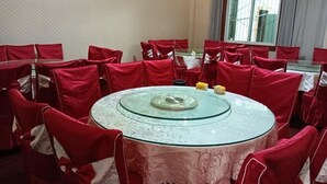 A round glass table with a white tablecloth, surrounded by red chairs with white sashes. - Reshuitang Hotel (Li County)