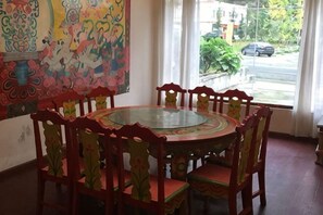 A round dining table with chairs, a colorful mural on the wall, and a view of the street outside.