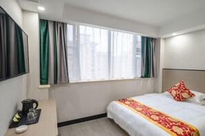 A hotel room with a bed, a desk with a coffee maker, and a window with curtains.