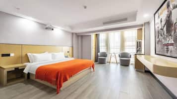Habitación de hotel con cama, mesita de noche, dos sillones, escritorio, ventana grande y un cartel en la pared.