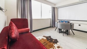 Une pièce moderne avec un canapé rouge, une petite table, un écran de projection et une grande fenêtre avec des rideaux.