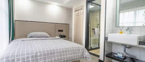 Una habitación de hotel moderna con una cama, una mesita de noche, un espejo y un baño con lavabo y ducha.
