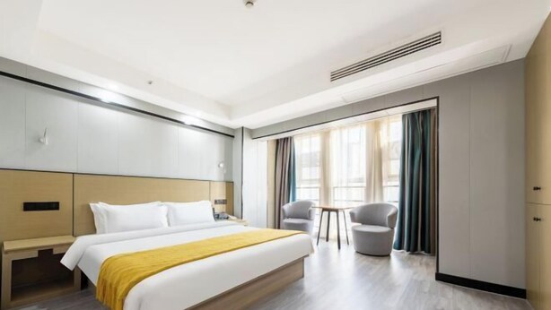 Une chambre d’hôtel moderne avec un grand lit, deux fauteuils, une petite table et une armoire.