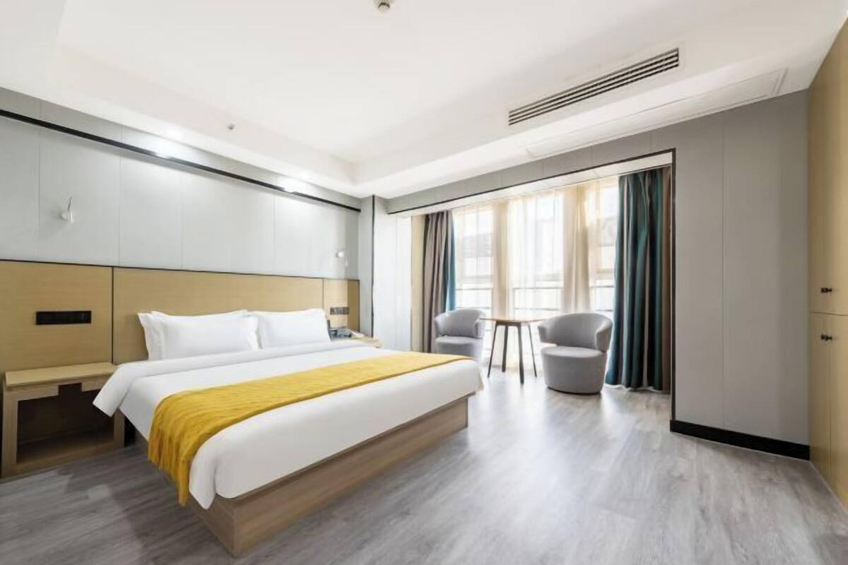 Une chambre d’hôtel moderne avec un grand lit, deux fauteuils, une petite table et une armoire.
