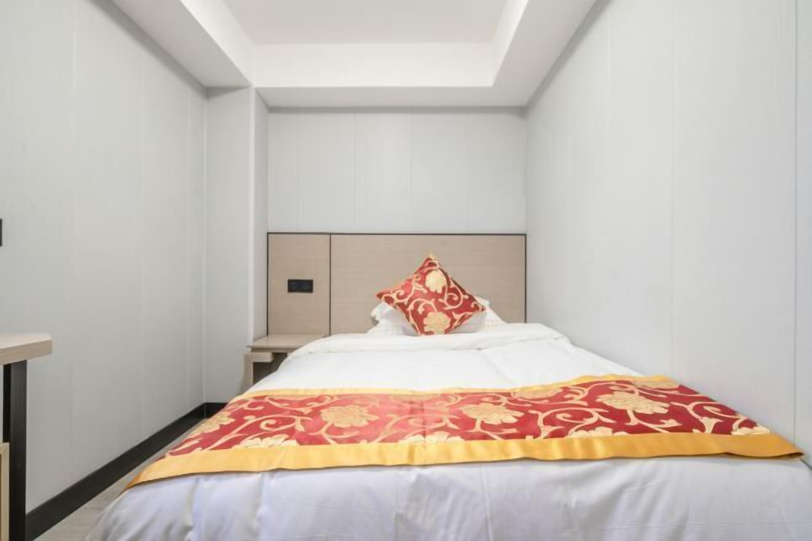 Una habitación de hotel estrecha con una cama, una mesita de noche y una pequeña mesa.