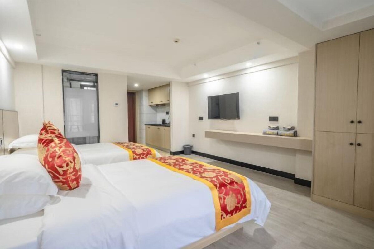 Ein Hotelzimmer mit zwei Betten, einem Fernseher, einer kleinen Küchenzeile und einem Kleiderschrank.