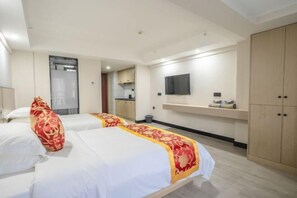 Ein Hotelzimmer mit zwei Betten, einem Fernseher, einer kleinen Küchenzeile und einem Kleiderschrank.