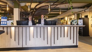A reception desk with two staff members, a modern interior with exposed beams, and a visible bar area. - Fletcher Hotel-Restaurant Marknesse (Marknesse)
