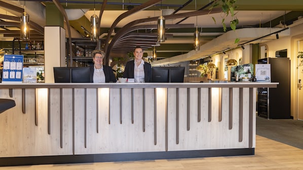 Una recepción con dos empleados, un interior moderno con vigas a la vista y un bar visible.