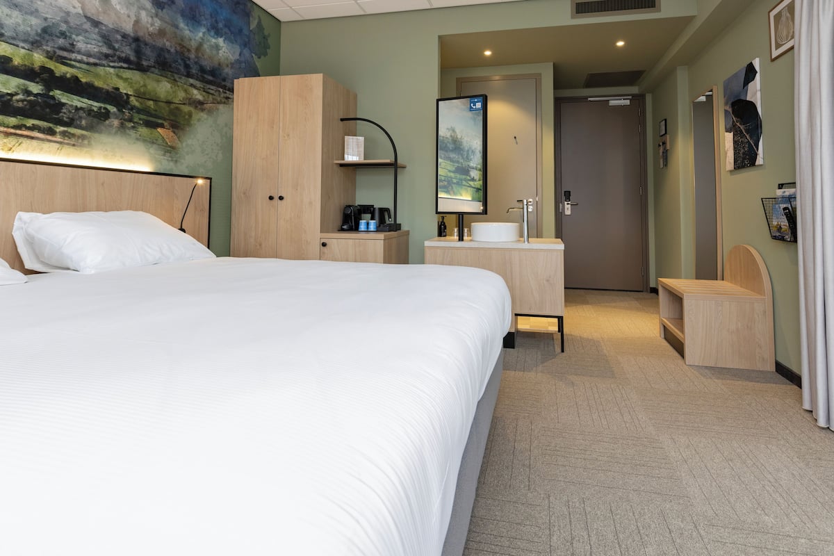 A hotel room with a large bed, a desk with a mirror, a coffee maker, and a painting on the wall.