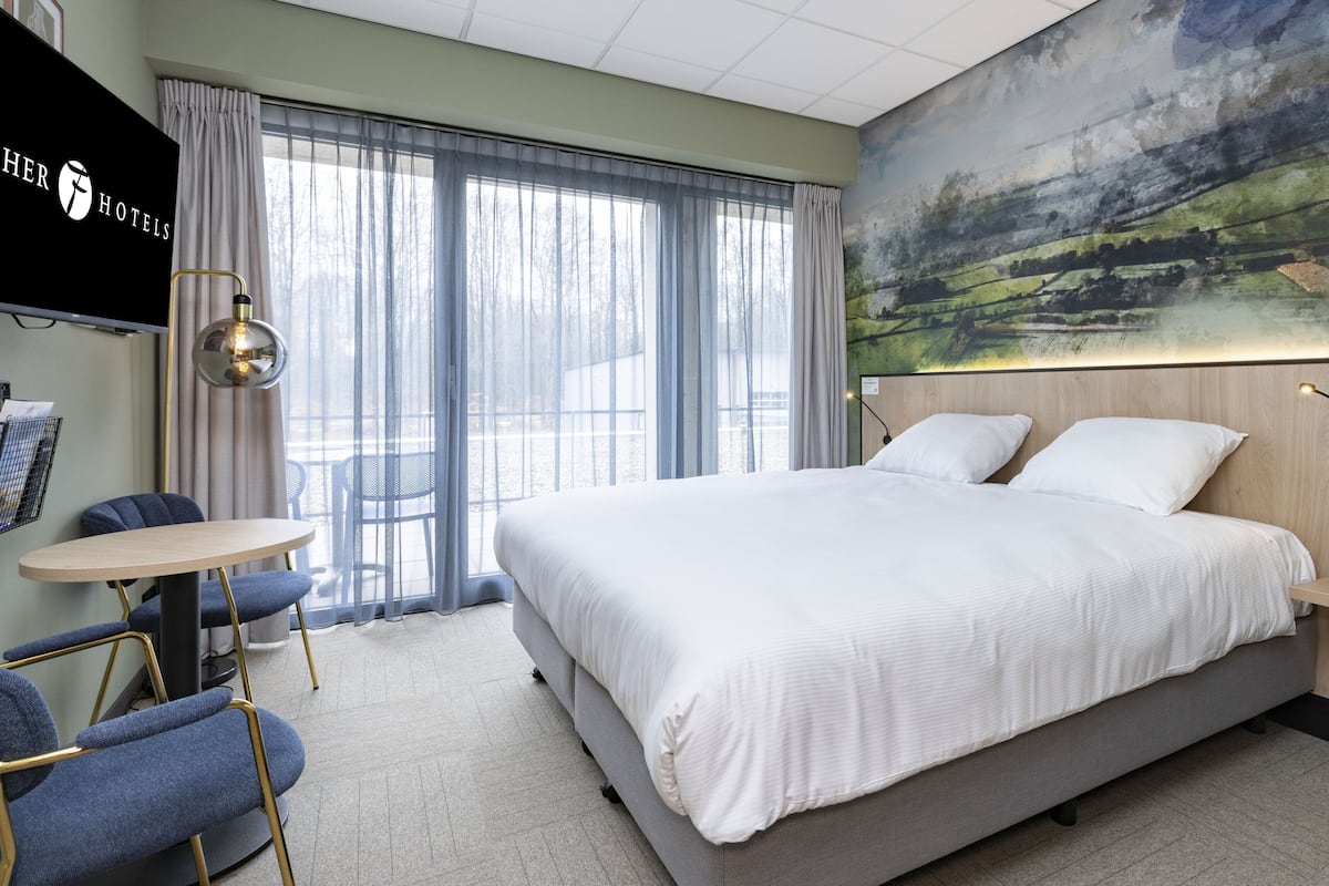 A hotel room with a large bed, a desk, chairs, and a painting on the wall.