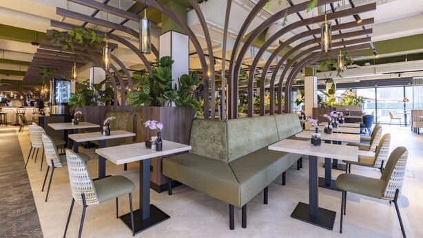 A modern restaurant interior with high ceilings, curved wooden beams, and a mix of seating options including tables and a central bench. - Fletcher Hotel-Restaurant Marknesse (Marknesse)
