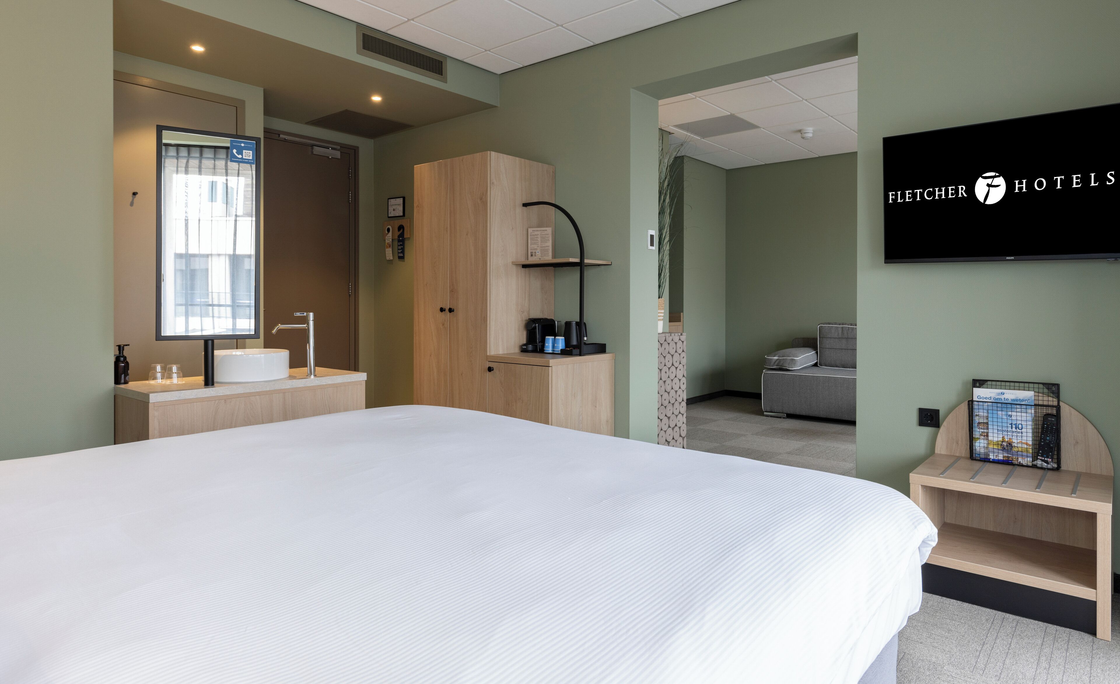 Hotelkamer met een groot bed, een wastafel, een spiegel, een kledingkast, een televisie en een klein tafeltje met dienblad.