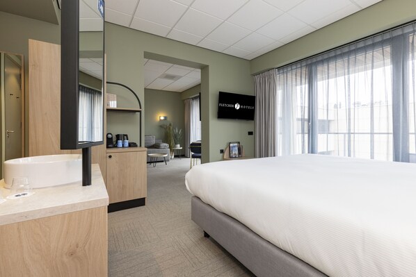Habitación de hotel con una cama grande, un escritorio de madera con lavamanos, un televisor de pantalla plana y vistas al exterior a través de amplios ventanales.