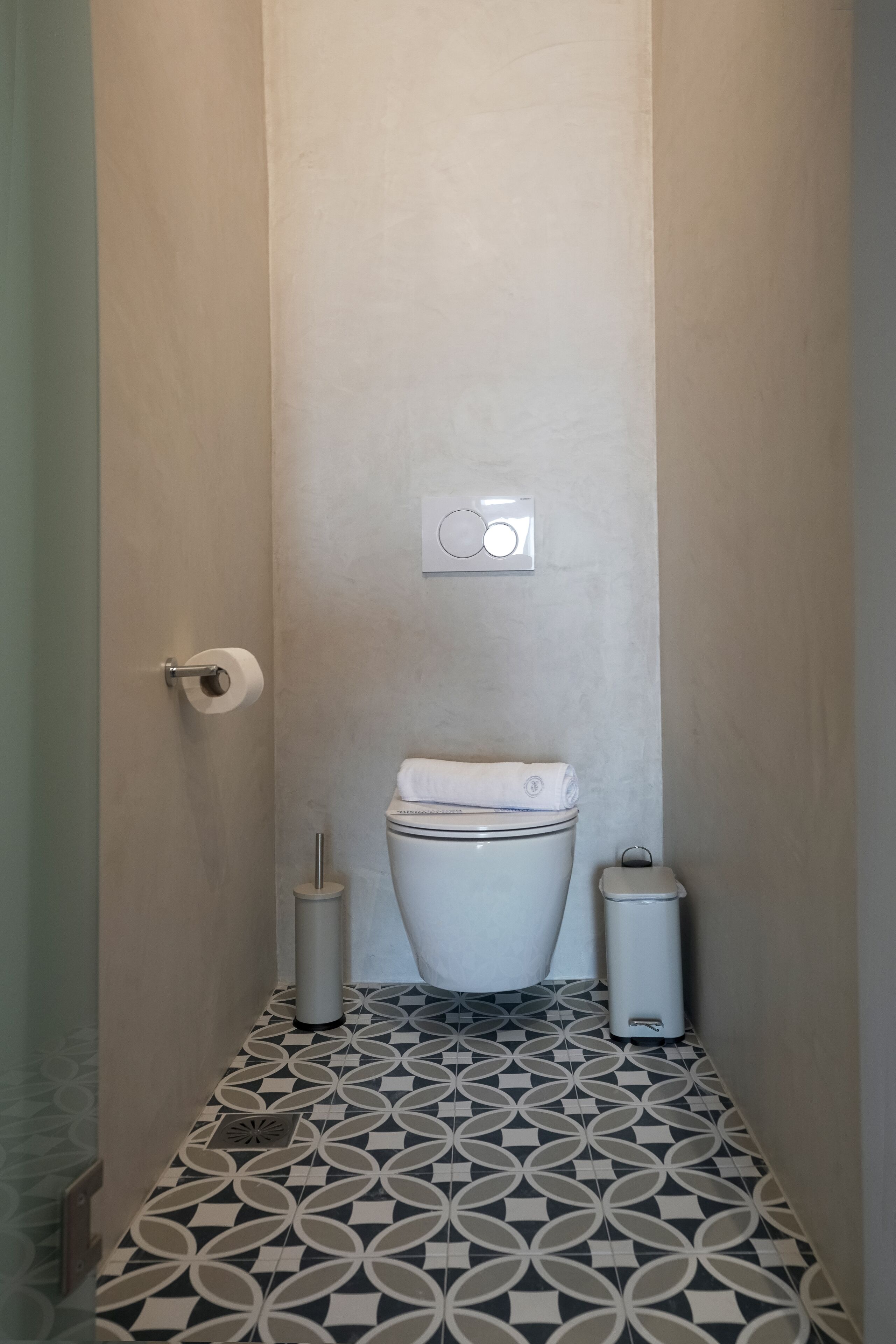 A narrow bathroom with a toilet, a trash bin, and a toilet paper holder.