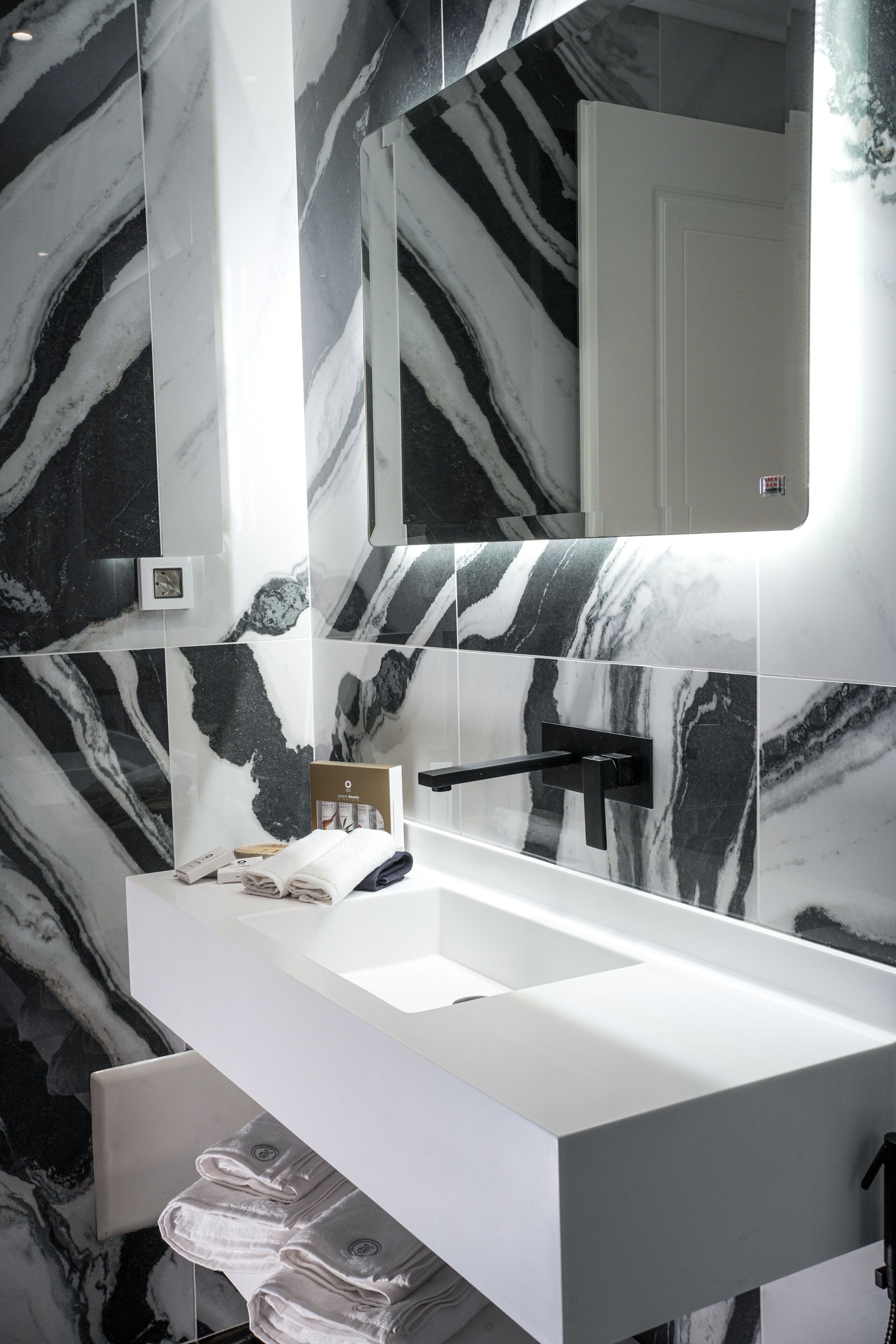 Un baño moderno con un lavamanos blanco, baldosas de mármol blanco y negro, un espejo y un perchero para toallas.