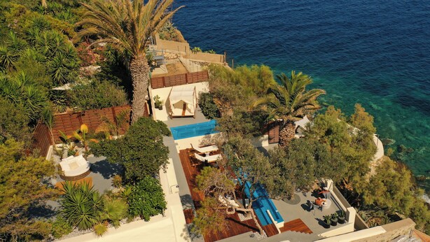 A coastal property with a swimming pool, outdoor seating, and lush vegetation. - Pafsilipon Suites (Syros)