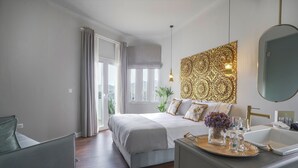 A modern bedroom with a large bed, a bedside table with a mirror, and a view of the city through the window. - Pafsilipon Suites (Syros)