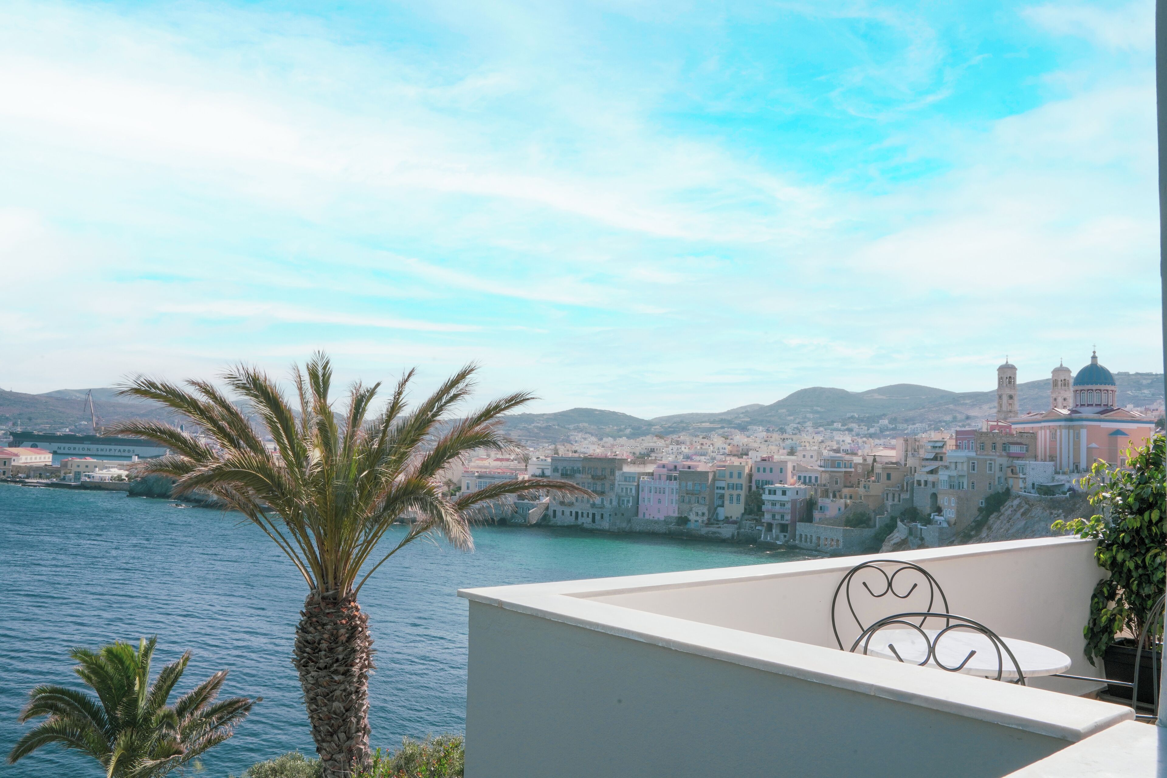 Un balcon avec vue sur une ville côtière, des palmiers et une étendue d’eau.