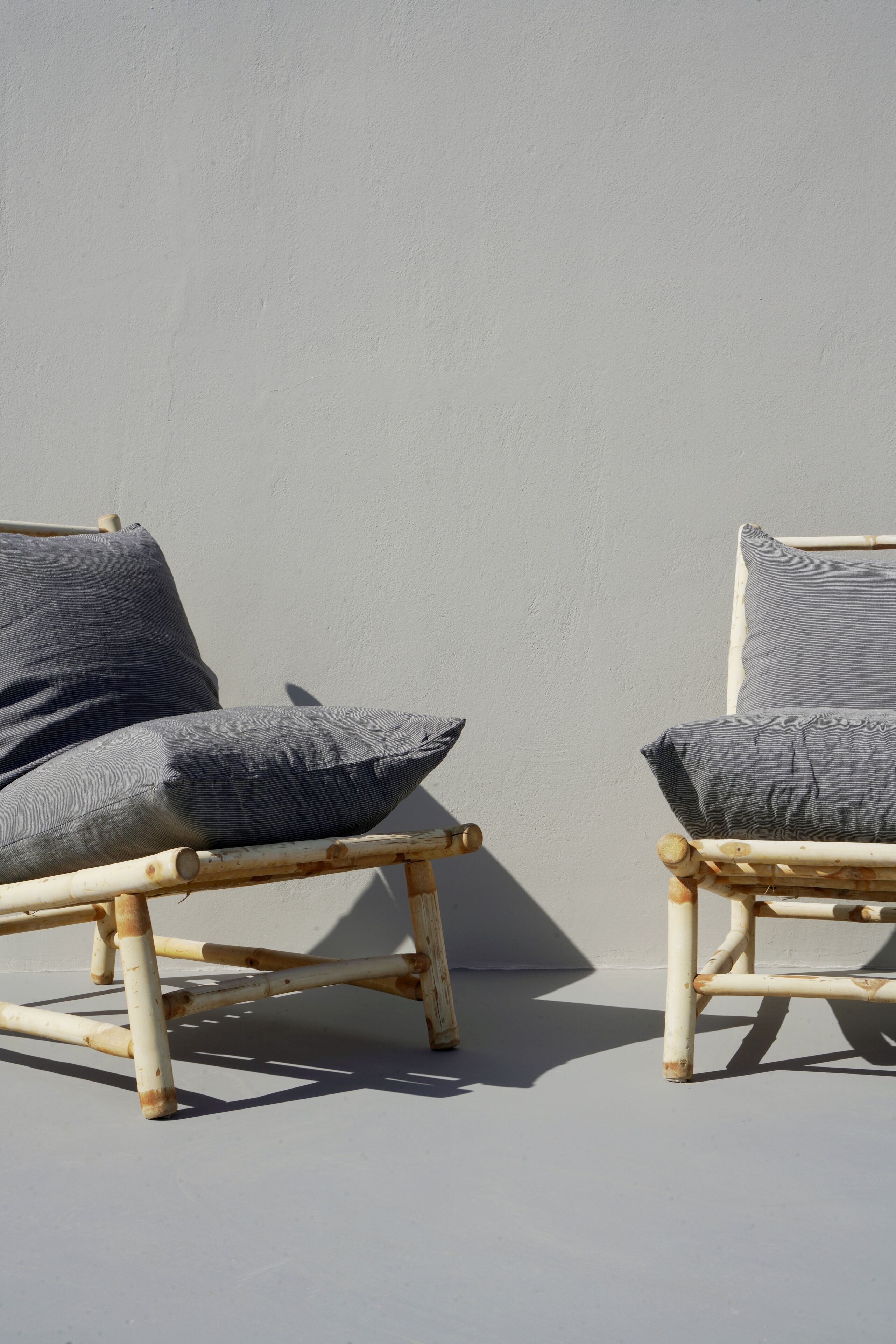 Twee rieten stoelen met grijze kussens voor een effen muur.