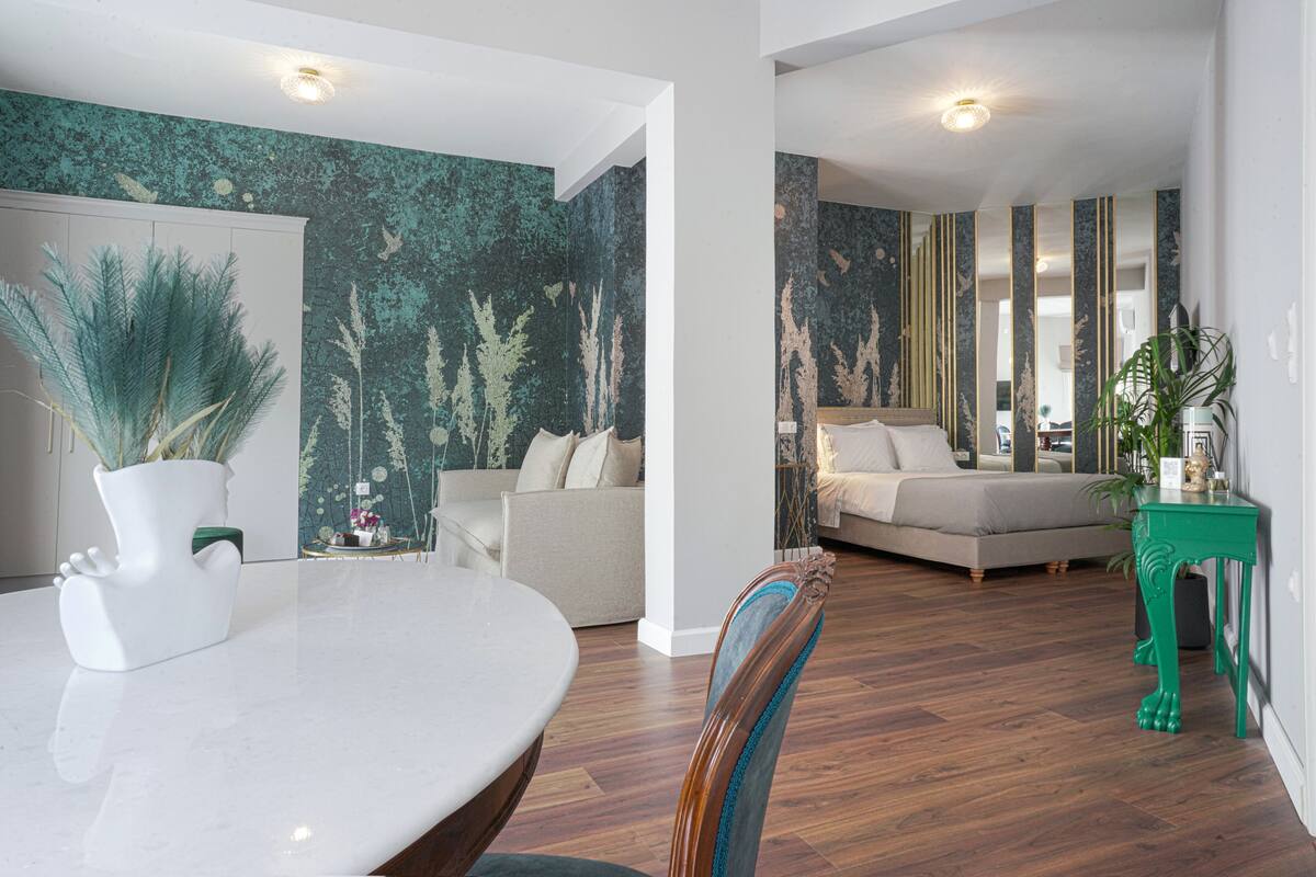 A modern living room with a sofa, a dining area with a table, and a green accent wall.
