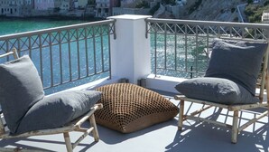 A balcony with two wicker chairs and a cushion, overlooking a coastal city with historic buildings and a church with a blue dome. - Pafsilipon Suites (Syros)